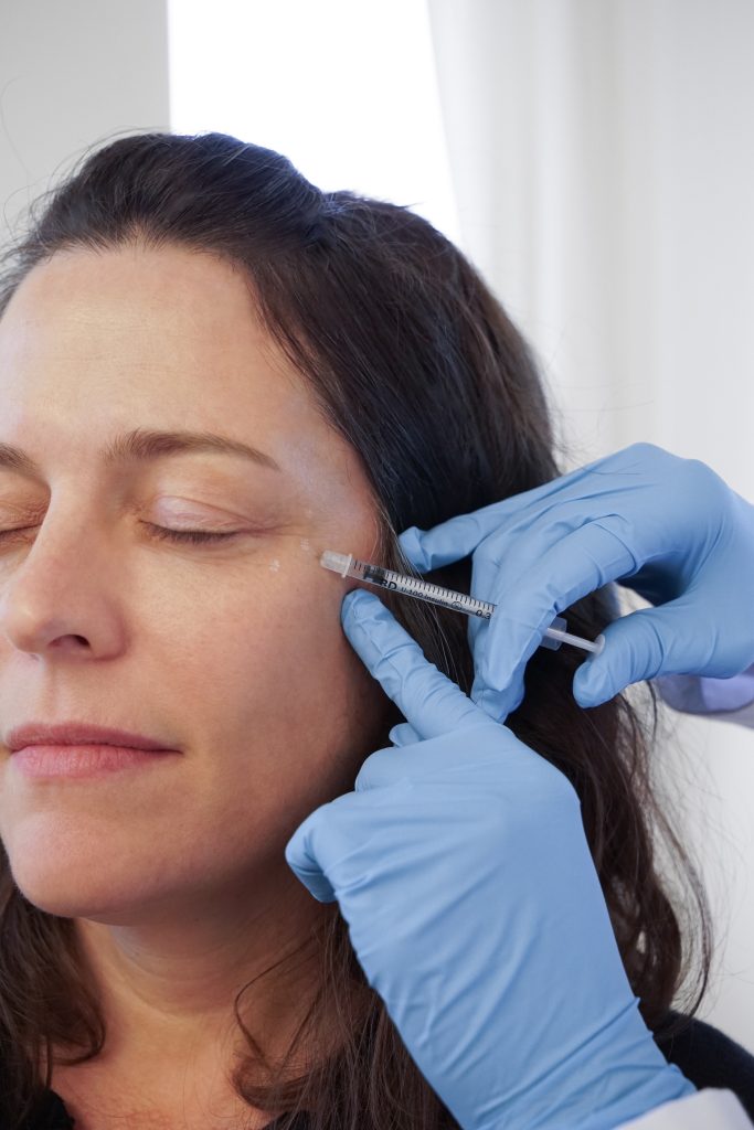 A patient receiving a cosmetic injection near the eye by a professional in a clean clinical environment.