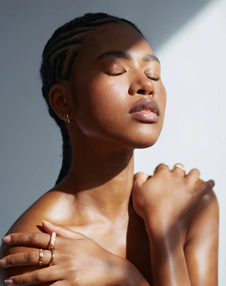 A close up shot of a woman with her arms rested against her shoulders. Her eyes are closed as the light hits her face. - Custom Facials in Marina Del Rey, CA